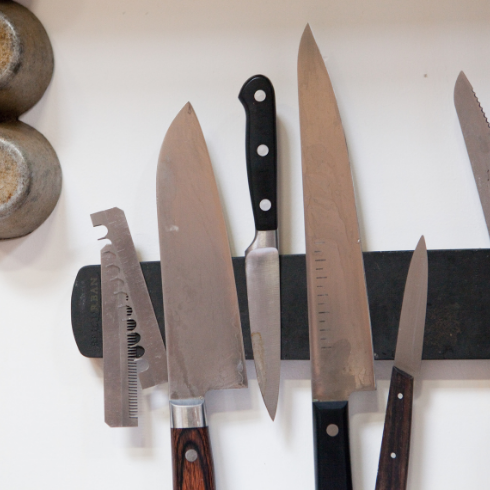 A wall-mounted magnetic strip holding an array of kitchen knives.