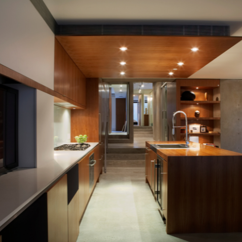 A sleek, modern kitchen with wood millwork, dark lower cabinets and recessed lights across the ceiling.