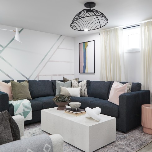 Basement with subtle white accent wall, blue sectional, white coffee table and black modern light
