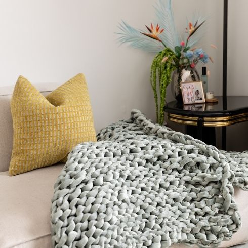 Yellow throw pillow and grey chunky-knit throw blanket on a cream couch