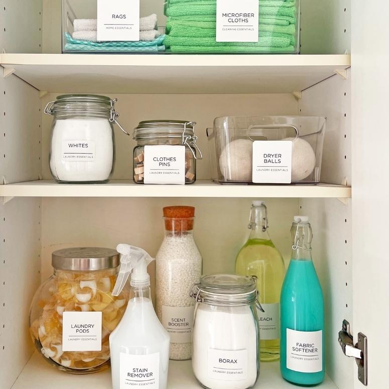 Labeled laundry items in glass canisters organized in a shelved cabinet.