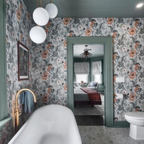 A floral-printed wallpaper, white soaker tub and sphere lighting