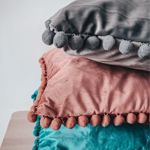 A stack of three pillows that are pink, blue and grey.
