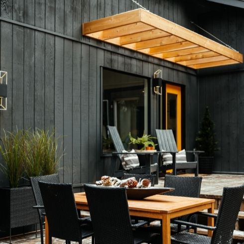 Outdoor patio of a black painted house, a wooden table and a yellow pergola