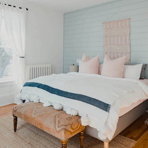A guestroom painted blue, a bed with white sheets and pink pillows