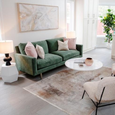 Living room with green velvet couch, tan area rug and white circular coffee table