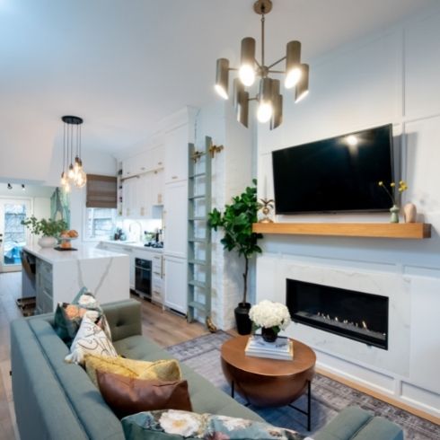 A living room and kitchen with a mounted TV, blue sofa, and modern light fixtures