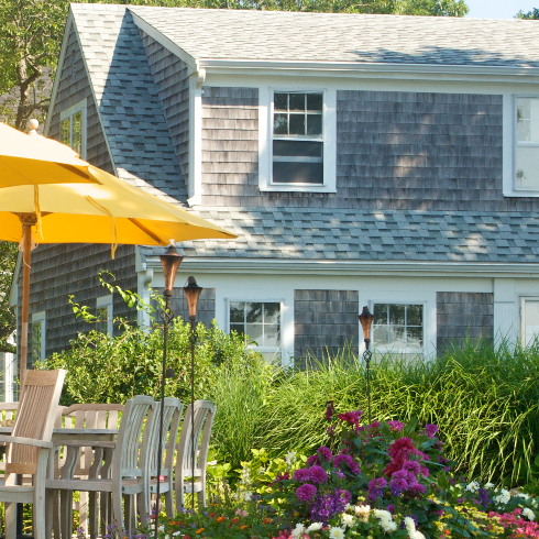 Exterior of a Cape Cod style home with grey shingles and a lush garden
