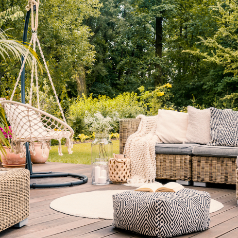 A black and white pouf in the middle of an outdoor living space with a rattan corner sofa, hanging chair and round rug