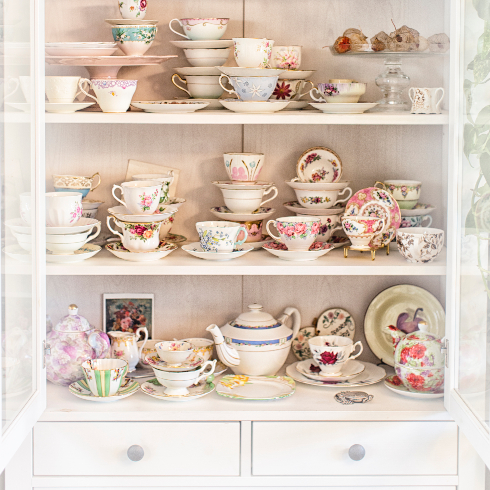 A white China cabinet filled with colourful plates, teacups, saucers and teapots.