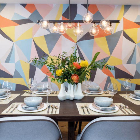 A dining room with a geometric, multi-coloured wallpaper on an accent wall.