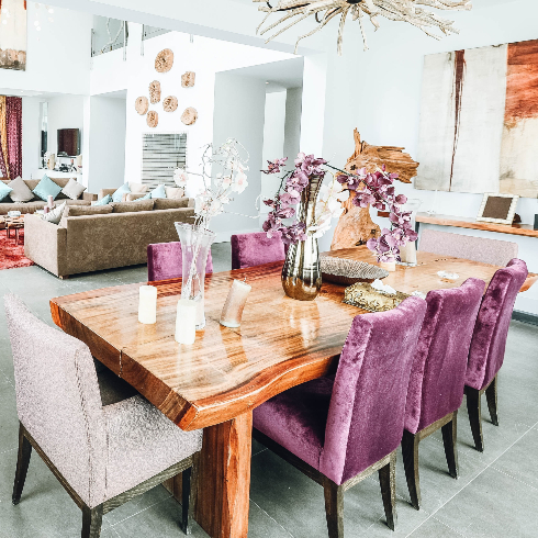 A wooden, live edge dining table with six purple chairs and two lavender chairs at either end