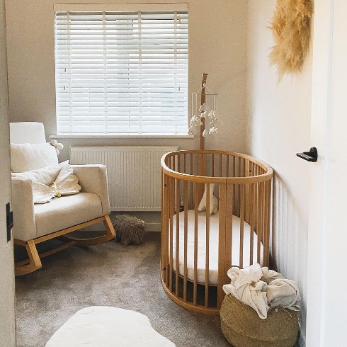 Nursery with beige walls, brown round crib and a white rocking chair.