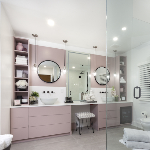 Contractor Sebastian Clovis and designer Sabrina Smelko built a sophisticated bathroom with pink and white walls, pink storage drawers, a white countertop, two vessel sinks, four pendant lights, two round mirrors, and a vanity stool as featured on HGTV Canada