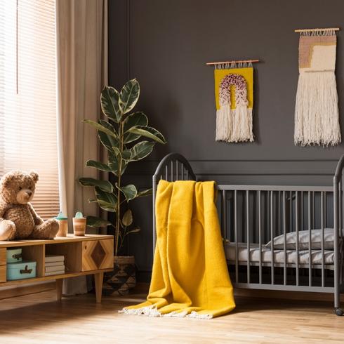Gender-neutral nursery with black painted walls, yellow blanket and green plant in the corner.