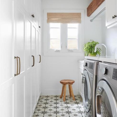 Narrow laundry room with white cupboards and white and black tile floor