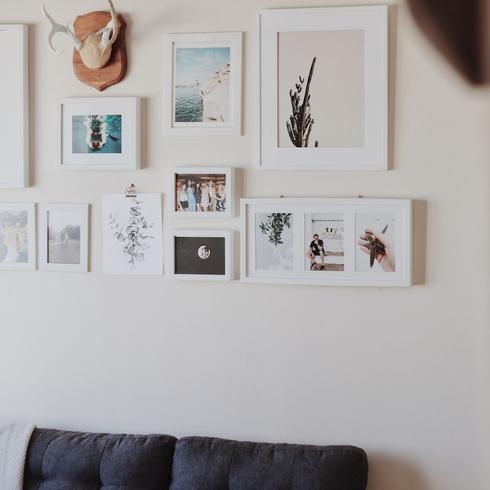 A gallery wall with white photos in white frames mounted on the wall.