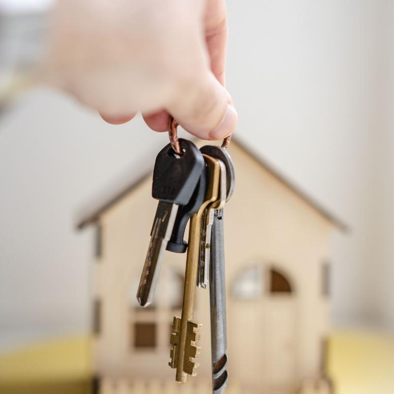 A person holding a set of keys in front of a cardboard house
