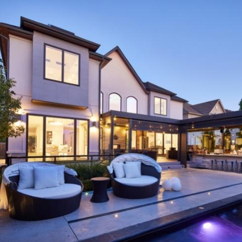 The exterior of a home with big windows from the view of the pool and backyard.
