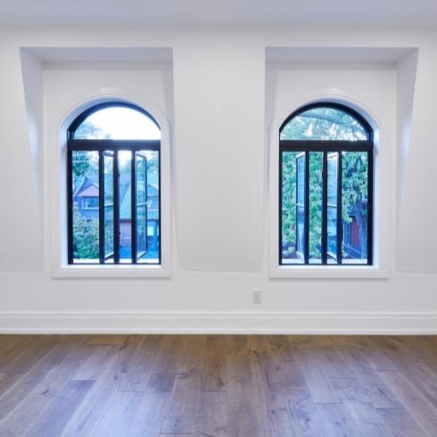 An interior view of an empty room with dark hardwood floors, white floors and a pair of two black arched windows.