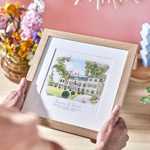 A person holding a custom illustration of a wedding venue in a frame