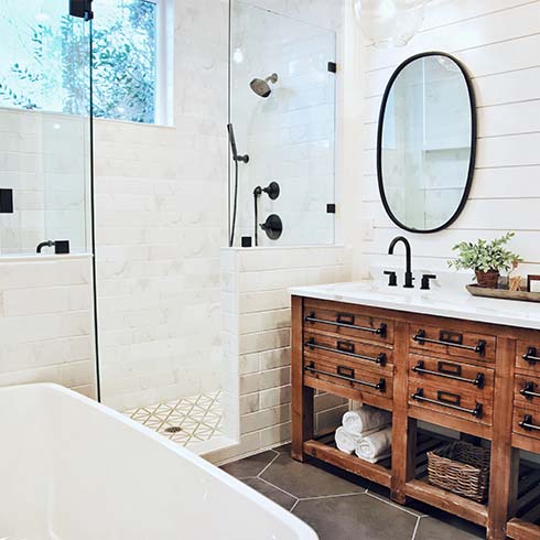 A bathroom with white walls, a wooden vanity, black mirrors and white bath tub.