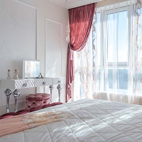 Bedroom painted white, with a silver makeup table and pink curtains.