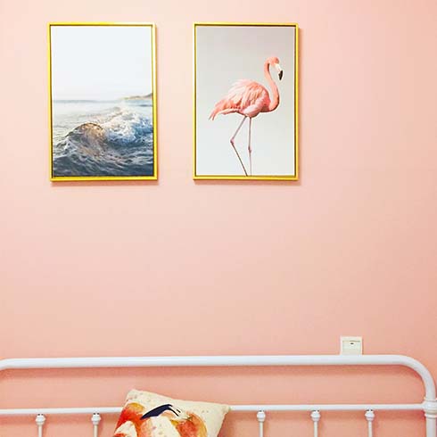 Blush pink room with two pieces of art above a white bed.