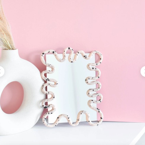 A squiggle-shaped mirror on a white ledge in a pink room.
