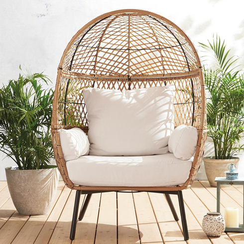 A rattan egg chair on a porch with white cushions.