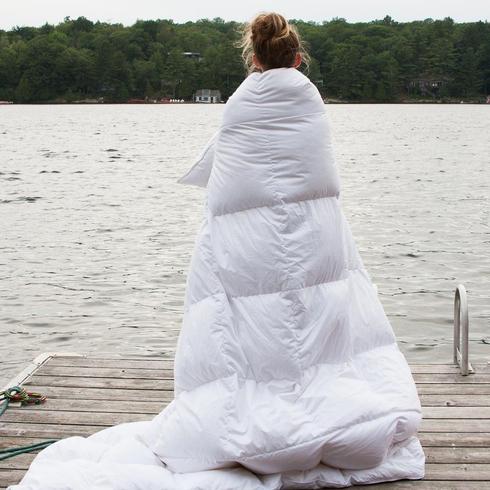 Woman with duvet cover overlooking lake.