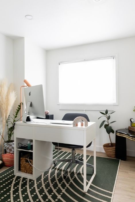 Office space with a white desk and a large silver desktop monitor, surrounded by large green house plants