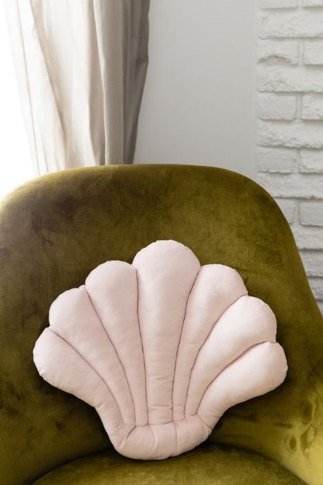 Green velvet arm chair with a light throw pillow in the shape of a shell