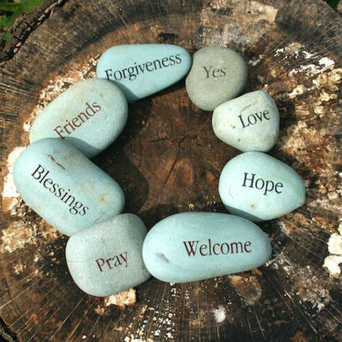 Eight river stones engraved with motivational words sit on a tree stump as part of a memorial garden