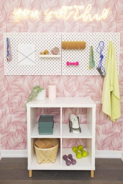 A wall with pink removeable wallpaper a neon sign, a pegboard and white shelf. 