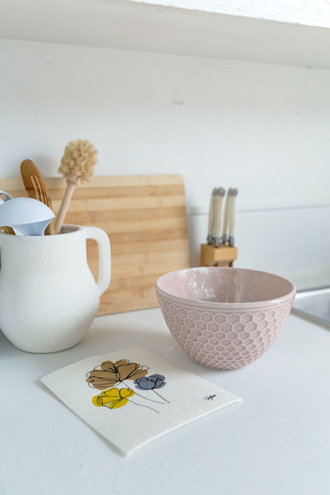 Goldilocks Goods Swedish dishcloth sits on a white kitchen counter surrounded by a pink bowl, white jug and wooden chopping board