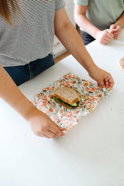 Goldilocks Goods team uses one of their beeswax wraps to wrap a sandwich on a white kitchen countertop 
