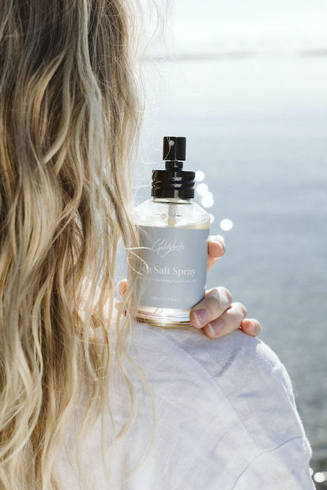Goldilocks Goods Sea Salt Spray sits on the shoulder of a model looking out to the ocean