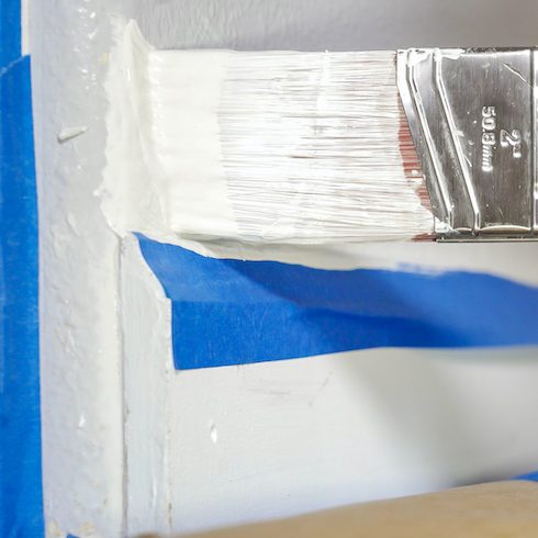 Close up of painter hands with gloves painting the wall edge with brush. Hand painting above molding, baseboard as part of a painting starter kit of essential tools