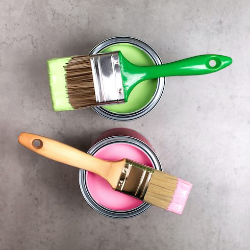 Paintbrushes on two metal bucket with green and pink pigments for renovation works on concrete grey background as part of a painting starter kit of essential tools
