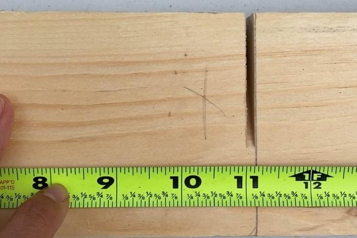 A person using a measuring tape against a piece of wood.