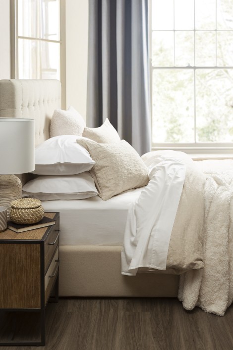 Light-coloured sustainable bedding with bedside table