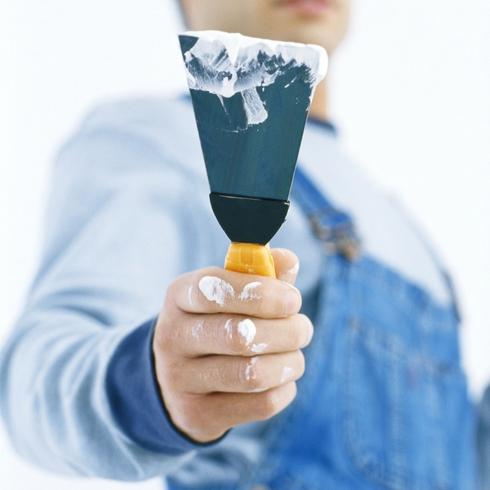 Worker holding out putty knife a tool included in painting kit of essential tools