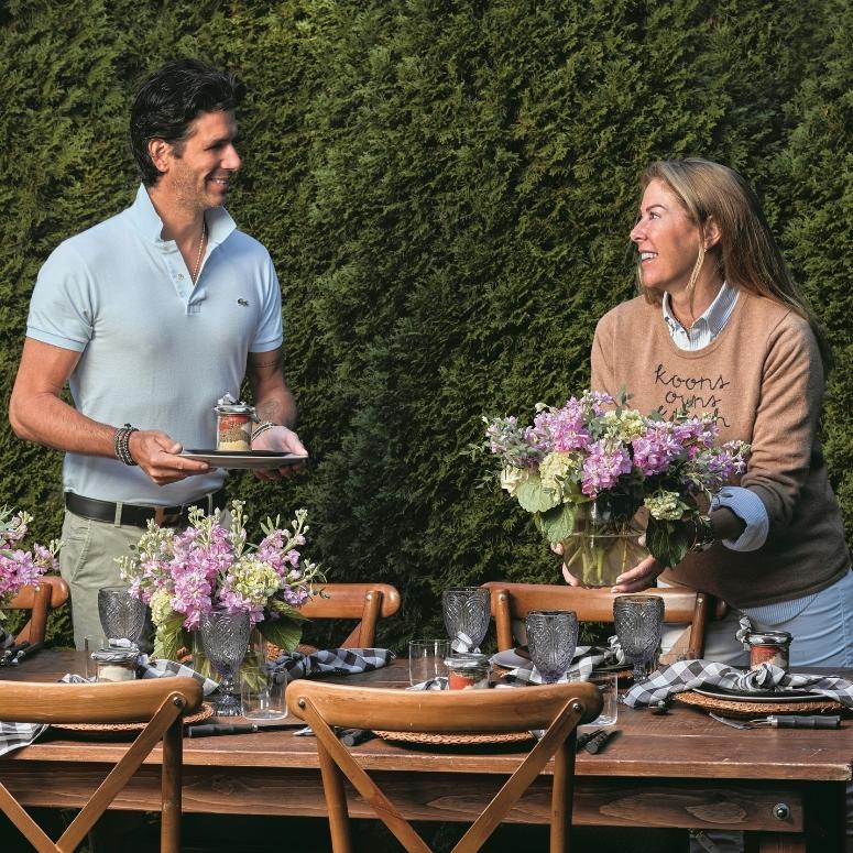 A couple smiling and setting up a table together for a dinner party.
