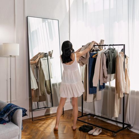 A woman arranging her clothes on a clothes rack.