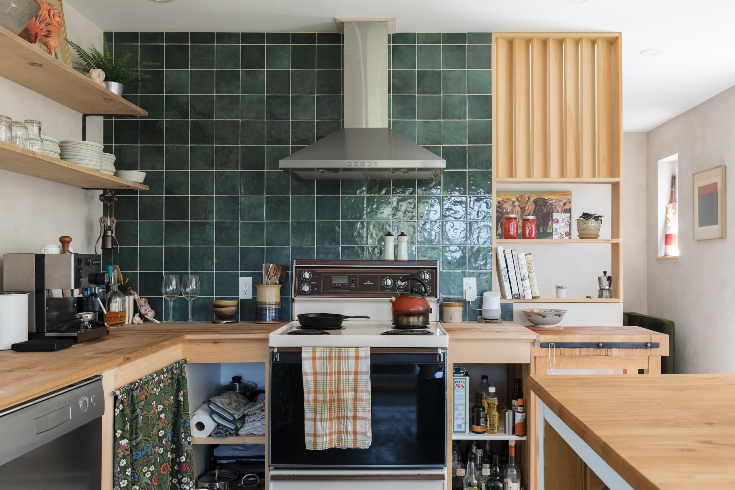 A kitchen with a vintage stove, wooden countertops and a bold green tile backsplash
