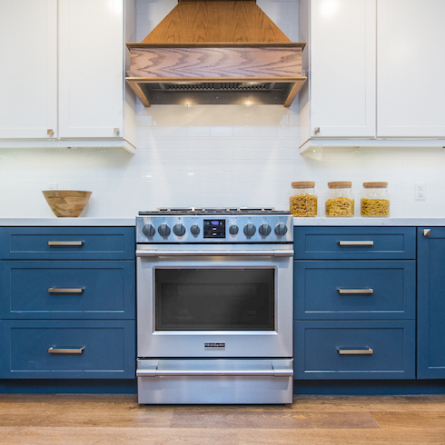 Bryan and Sarah Baeumler designed this beautiful kitchen featuring white upper cabinets and tranquil blue lower cabinets, wood floors and a wooden stove hood, and a white tile backsplash as part of a home reno trends story for HGTV Canada