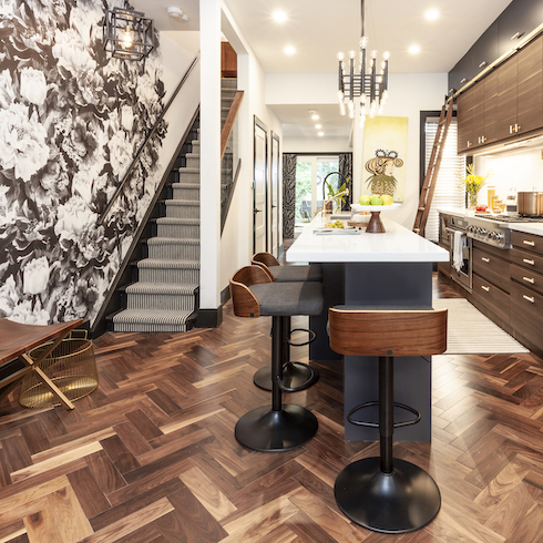 An opulent kitchen renovation by Save My Reno featuring a glass bannister and striped runner, a bold black-and-white floral wallpaper over the entire entry, dark herringbone parkay flooring, wood veneer bar stools and dark cabinets wall as part of a home reno trends story for HGTV Canada