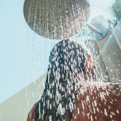 Low angle view of a woman in an outdoor rain shower as part of a home reno trends story for HGTV Canada