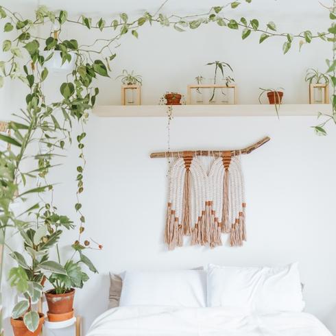 White bedroom with a vine, wooden shelf and macrame wall hanging